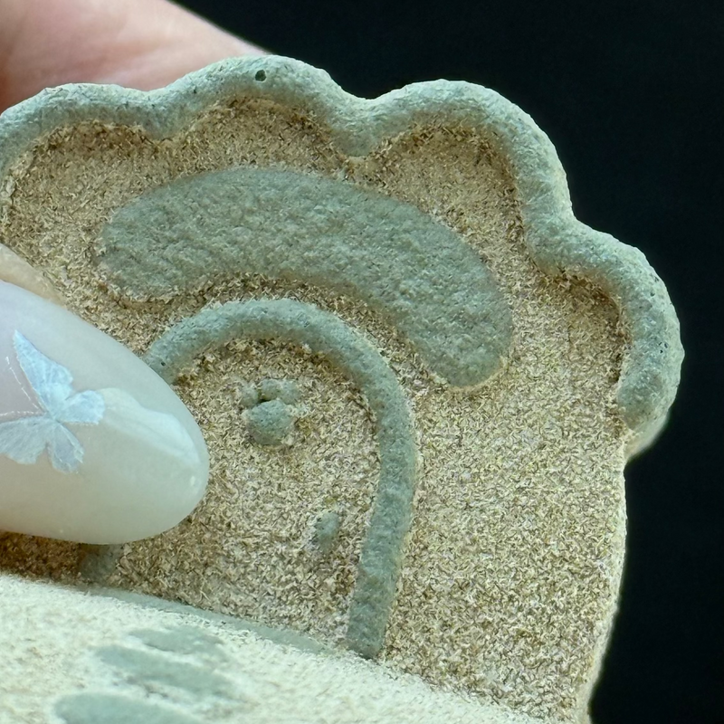 A close-up of a hand pressing a textured, beige pet urn