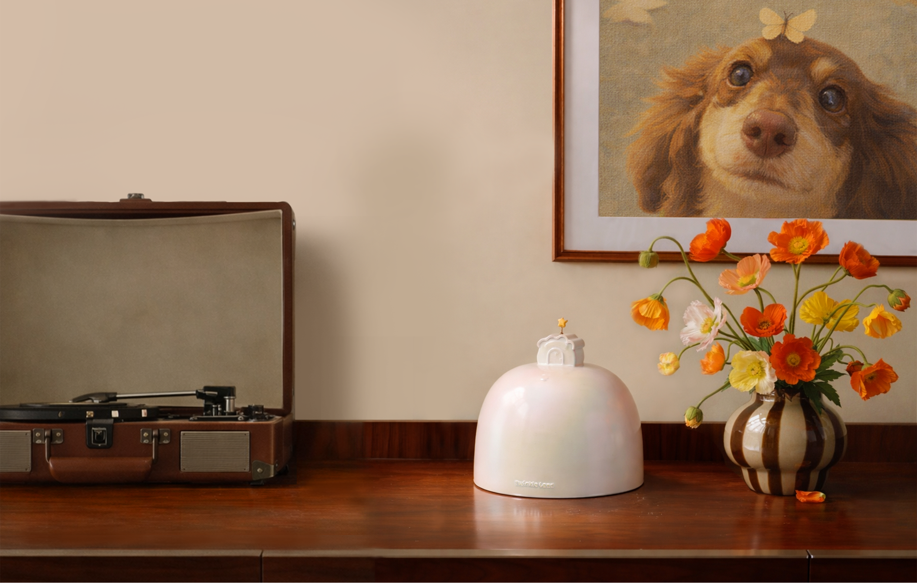 Vintage record player on a wooden surface with a vase of flowers, a pet urn and a framed picture of a dog on the wall.