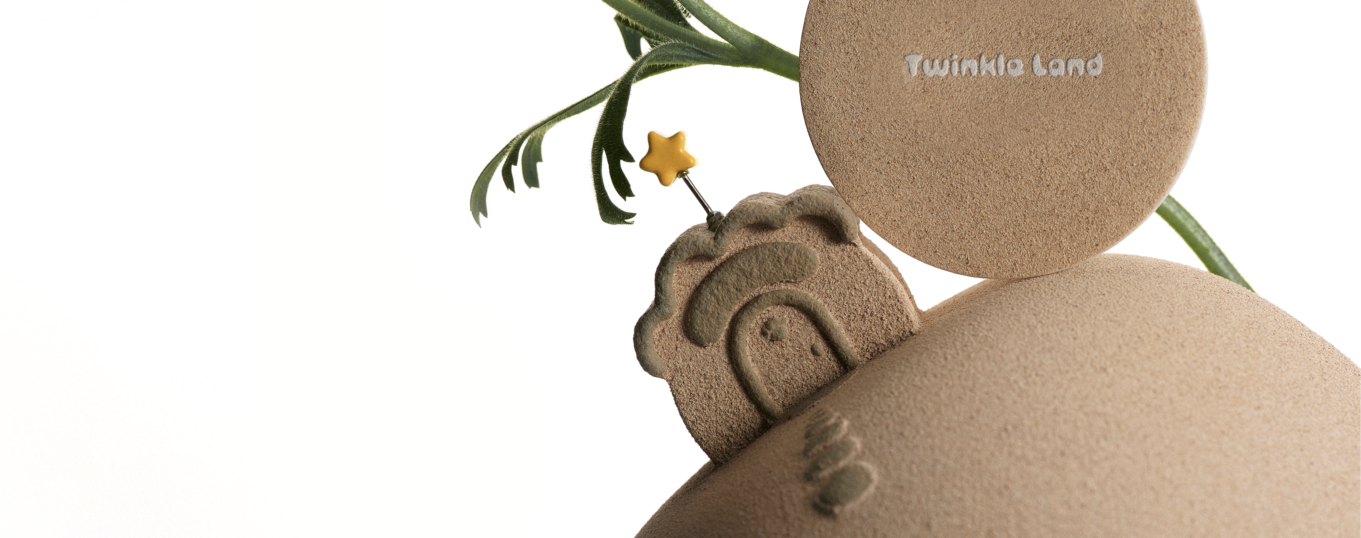 A close-up of a textured beige circular pet urn with the brand name 'Twinkle Land' embossed on it, alongside a matching embossed house shape and green stem accents on a white background.